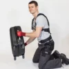 Mann mit Exoskelett hebt knieend mit Leichtigkeit einen Koffer hoch