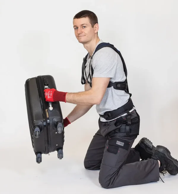 Mann mit Exoskelett hebt knieend mit Leichtigkeit einen Koffer hoch