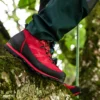 Ein roter Haix Ramble GTX-Schuh an einem Fuß, der auf einem moosbewachsenen Ast steht, umgeben von grünem Laub im Wald.
